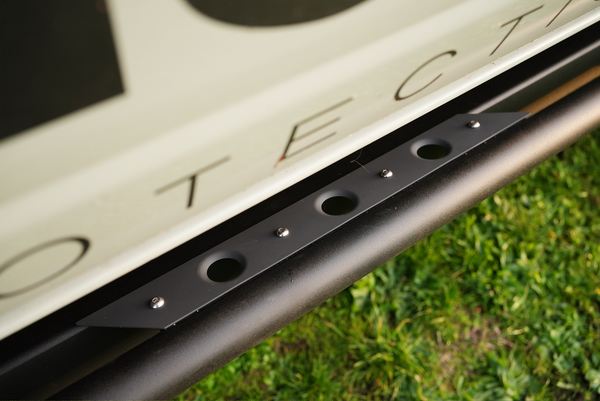 Close-up of black metal Sidewinder rock slider mounted under 2021 Bronco 4-door side panel on grass background.