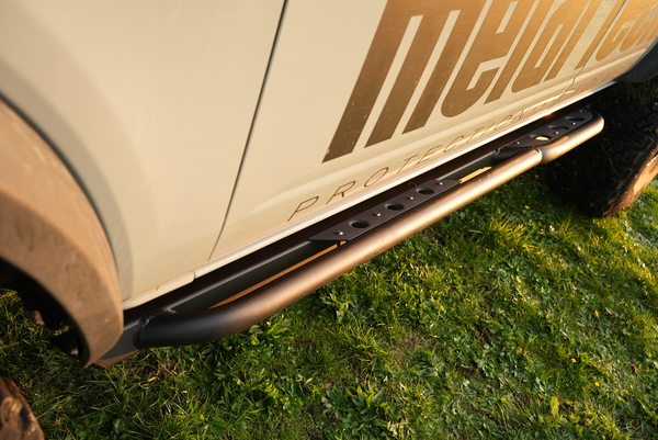 Close-up of black Sidewinder rock sliders installed on the side of a 2021 Bronco 4-door on grass.