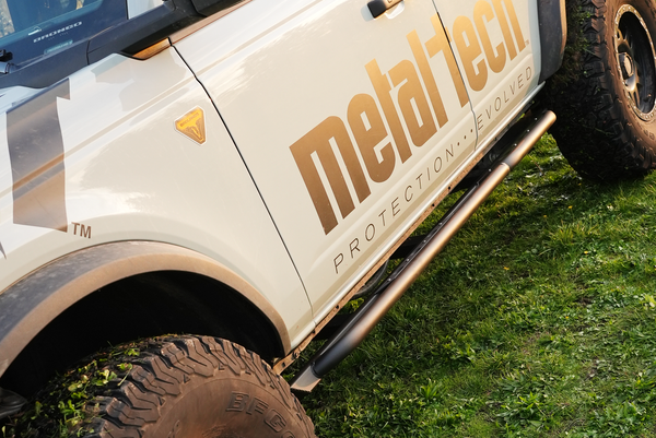 Close-up of 2021 Bronco 4-door with Sidewinder rock sliders installed on the driver side above off-road tires.
