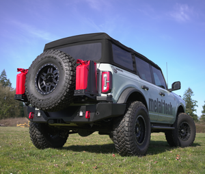 Rear view of a white Bronco 6G with Metal Tech 4x4 high rear bumper, spare tire, and red fuel cans mounted.