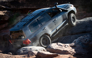 Black Toyota Land Cruiser climbing rocks, showing Metal Tech 200 Series rock sliders installed on the side.