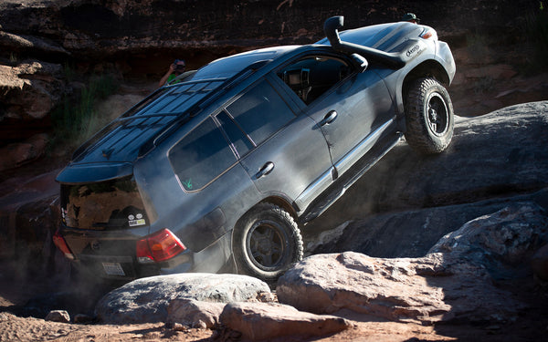Black Toyota Land Cruiser climbing rocks, showing Metal Tech 200 Series rock sliders installed on the side.