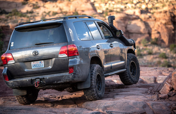 Rear side view of a Toyota Land Cruiser with Metal Tech 200 Series rock sliders on rocky terrain.