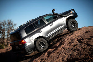Silver 200 Series Toyota Land Cruiser climbing rocky terrain with Metal Tech rock sliders installed on side rails.