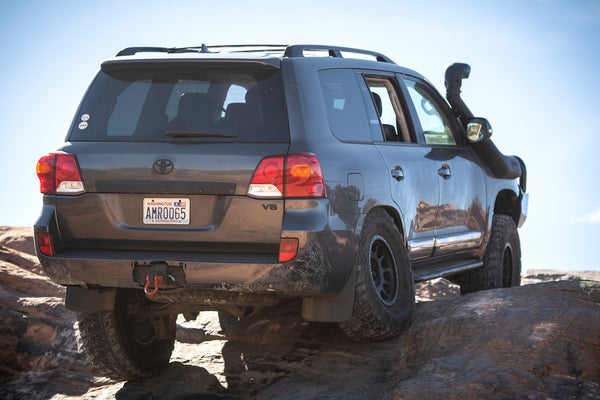 Rear side view of a Toyota Land Cruiser 200 Series with Metal Tech rock sliders, off-road on rocky terrain.