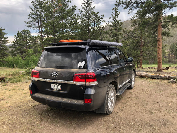Black Toyota Land Cruiser with Metal Tech 200 Series rock sliders installed, parked in a forested outdoor area.