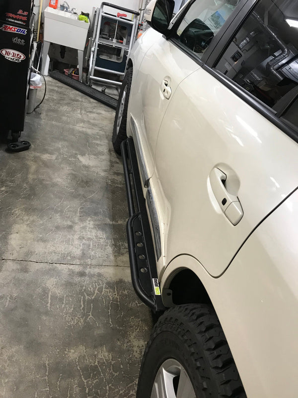 Black Metal Tech 200 Series rock sliders installed on white 2008-2021 Toyota Land Cruiser side view in garage.