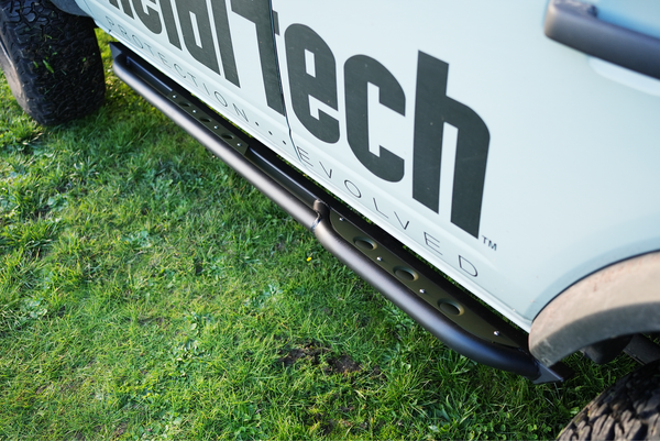 Close-up of black Sidewinder rock slider installed on the side of a white 2021 Bronco 4-door on grass.