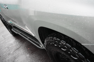 Close-up of black Metal Tech 4x4 rock slider installed on silver Lexus LX570 with wet pavement background.