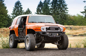Orange Toyota FJ Cruiser with Metal Tech Phantom front bumper installed, off-road tires, and open driver door outdoors.