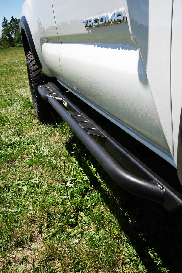 Close-up of black metal side slider installed on white 2016 Toyota Tacoma Access Cab, showing textured step surface.