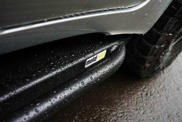 Close-up of wet black Metal Tech 4x4 rock slider installed on Lexus LX570 side near rear tire.
