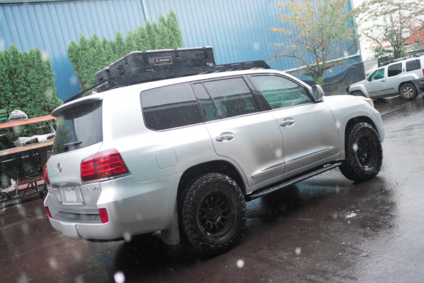 Silver Lexus LX570 with Metal Tech 4x4 black rock sliders installed, shown in rainy outdoor setting from rear side angle.