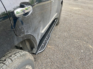 Close-up of black metal rock slider installed on the side of a black Lexus LX570 with off-road tires.