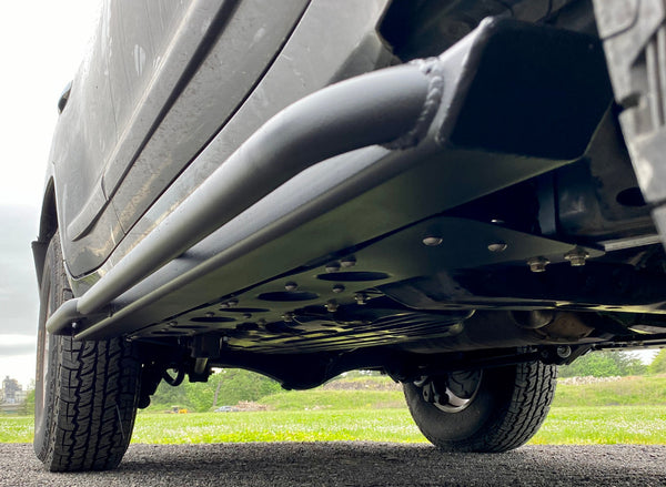 Close-up of metal rock slider installed on the side underbody of a Lexus LX570, showing mounting bolts and frame.