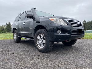 Black Lexus LX570 with installed Metal Tech 4x4 rock sliders and snorkel, parked on gravel outdoors.