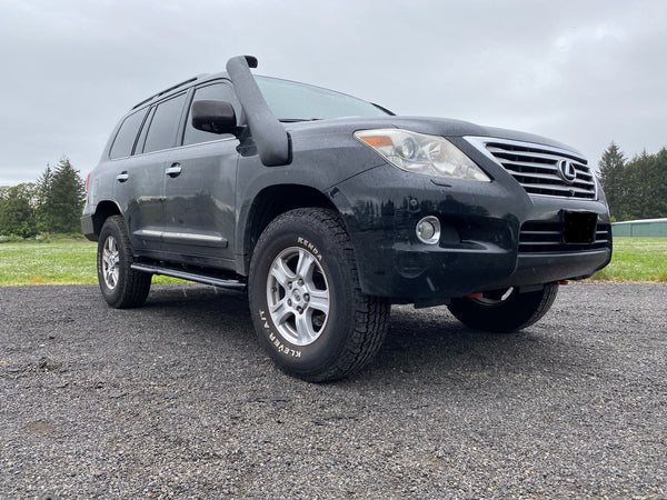 Black Lexus LX570 with installed Metal Tech 4x4 rock sliders and snorkel, parked on gravel outdoors.