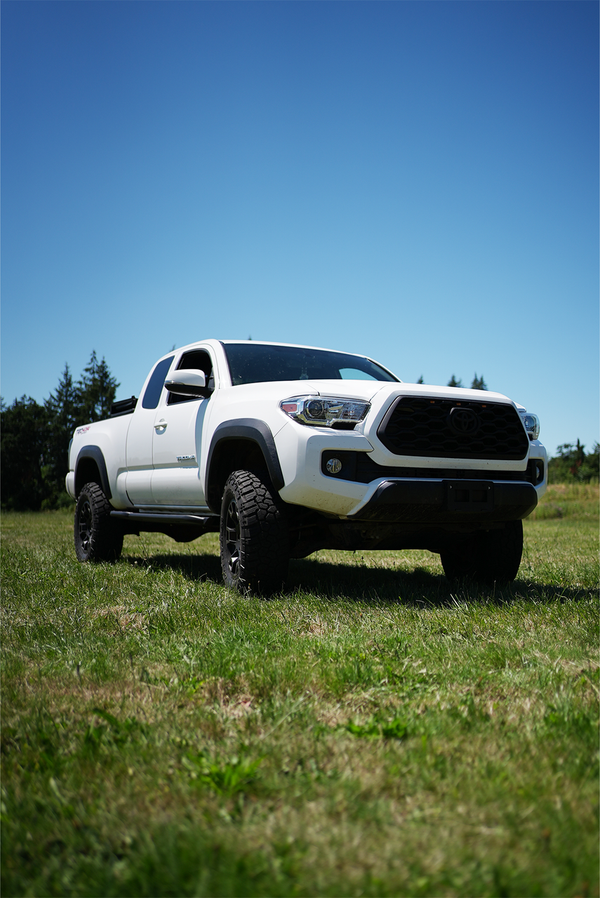 White 2016 Toyota Tacoma Access Cab with Metal Tech black side sliders on grass under clear sky.