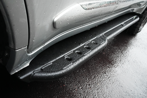 Close-up of black Metal Tech 4x4 rock slider installed on silver Lexus LX570, wet from rain, showing textured surface and mounting.