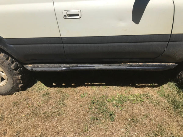 Side view of black Metal Tech 4x4 rock slider installed on white 80 Series Land Cruiser LX450 on dry grass.