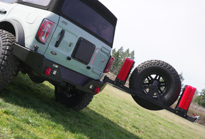 Rear view of Ford Bronco with black Ace of Hearts swing arm system holding spare tire and red fuel cans.
