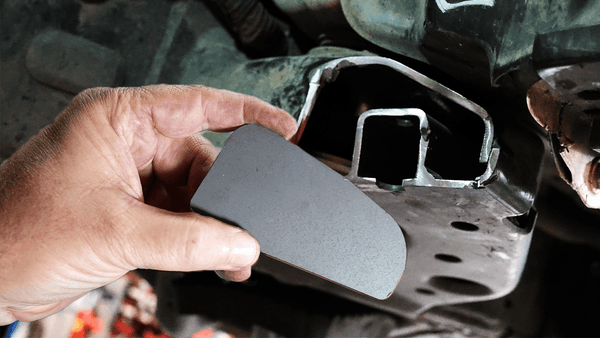 Hand holding a metal body mount chop plate near the frame of a 2014 4Runner for installation.