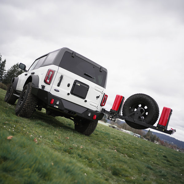 White Ford Bronco 6G with black Ace of Hearts swing arm system and rear bumper, mounted spare tire and red fuel cans.
