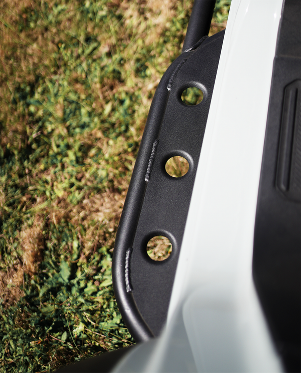 Close-up of black steel rock slider with circular cutouts installed on 2021 Ford Bronco 4-door near white vehicle body.