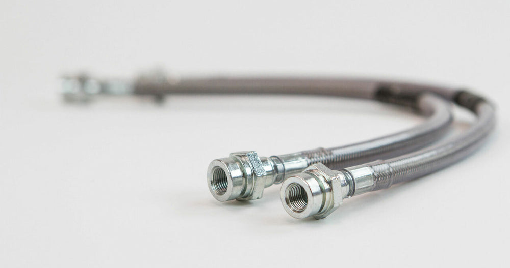 Pair of black extended rear brake lines with metal fittings and five metal clips on white background.