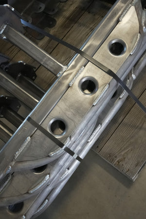 Close-up of raw metal Lexus GX470 rock slider with visible welds and mounting brackets on wooden floor.