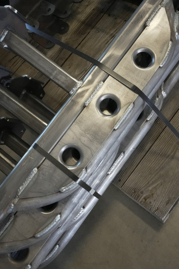 Close-up of raw metal Lexus GX470 rock slider with visible welds and mounting brackets on wooden floor.