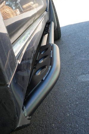 Close-up of black metal rock slider installed on 2010-2013 Toyota 4Runner side panel near rear tire.
