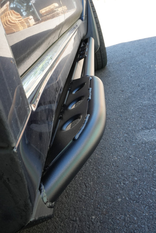 Close-up of black metal rock slider installed on 2010-2013 Toyota 4Runner side panel near rear tire.