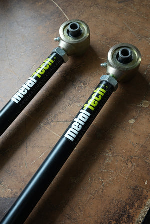 Pair of black Metal Tech rear upper suspension links with gold rod ends, shown on a brown surface.