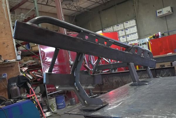Close-up of black metal rock slider for 80 Series Land Cruiser LX450, showing welds and mounting brackets in workshop.
