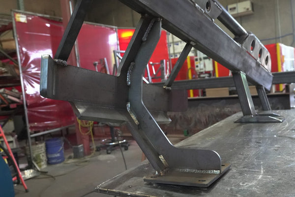Close-up of metal rock slider bracket with welds, designed for 80 Series Land Cruiser LX450, on workshop table.