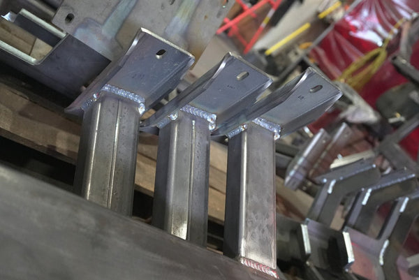 Close-up of welded metal brackets for 80 Series Land Cruiser LX450 rock sliders in workshop setting.