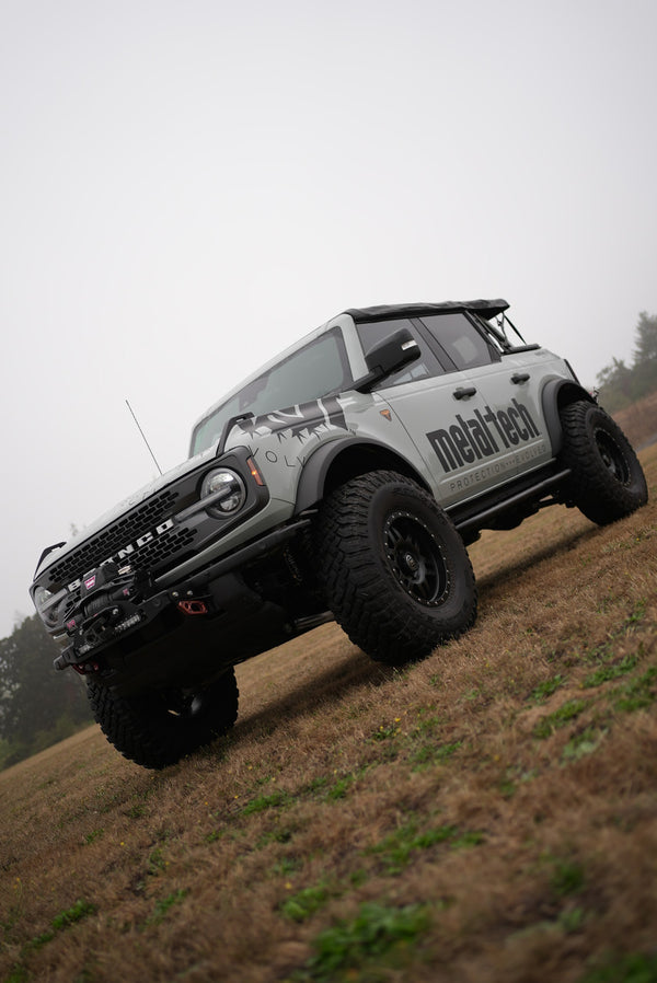 2021 Ford Bronco 4-door with Metal Tech rock sliders installed, shown from front side on grassy terrain.
