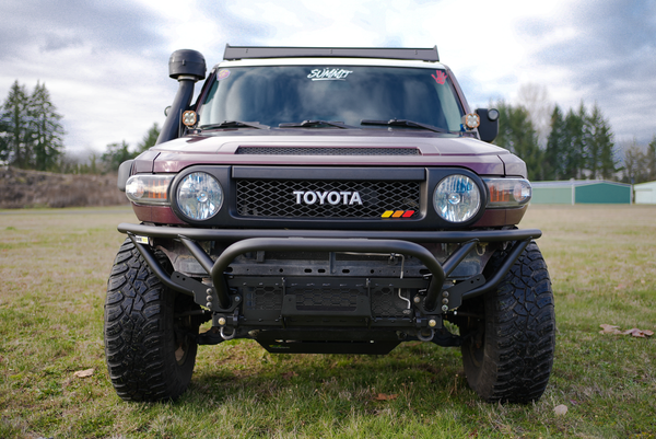 Front view of a Toyota FJ Cruiser with a black Metal Tech front tube bumper installed on grassy terrain.