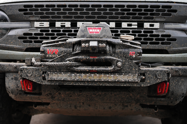 Close-up of a mud-covered Bronco 6G Stronghold winch mount with Warn VR Evo winch installed on front bumper.