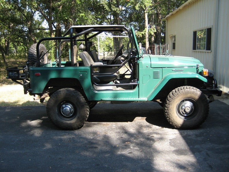 Green FJ40 Land Cruiser with Metal Tech Jackson pre-built roll cage, open doors, and off-road tires side view.