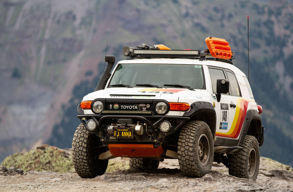 White Toyota FJ Cruiser with Metal Tech front tube bumper, off-road tires, and roof rack on rocky terrain.