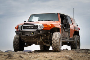 Orange Toyota FJ Cruiser equipped with Metal Tech Phantom front bumper on rocky off-road terrain.
