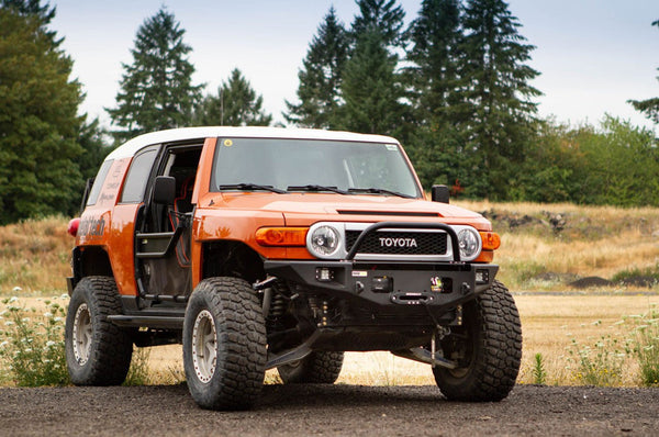 Orange Toyota FJ Cruiser with Metal Tech Phantom front bumper installed, off-road tires, and open driver door.