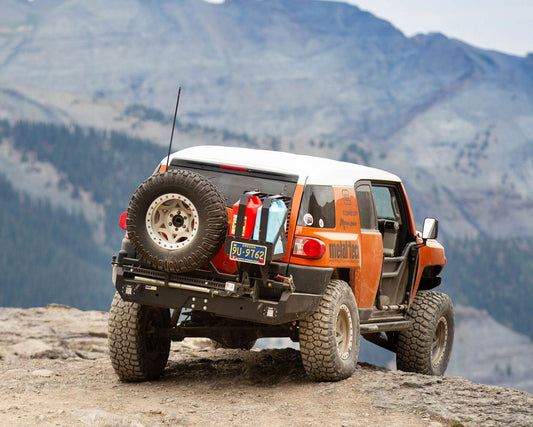 Rear view of FJ Cruiser with Metal Tech Red Eye II full shell rear swing-out bumper and mounted spare tire on rocky terrain.