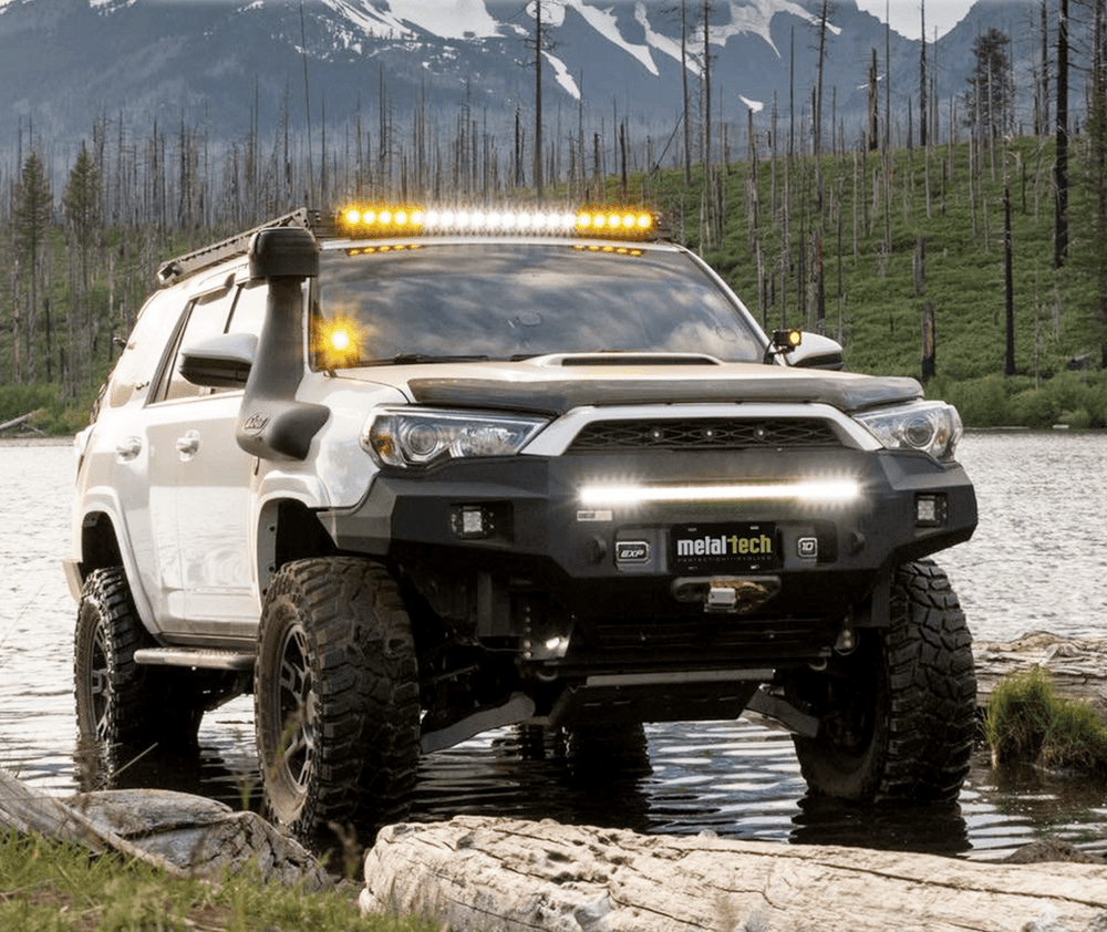 White 5th Gen 4Runner with Metal Tech Fortress front bumper and off-road lights, parked in shallow water outdoors.