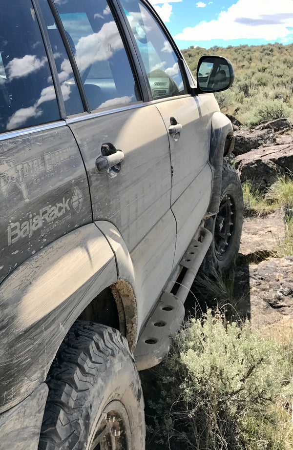 Close-up side view of dusty Lexus GX470 with Metal Tech 4x4 rock sliders installed on rocky off-road terrain.