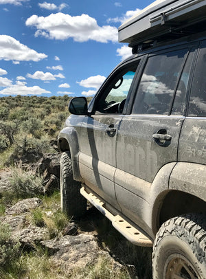 Side view of muddy Lexus GX470 with Metal Tech 4x4 rock sliders installed on rocky off-road terrain.