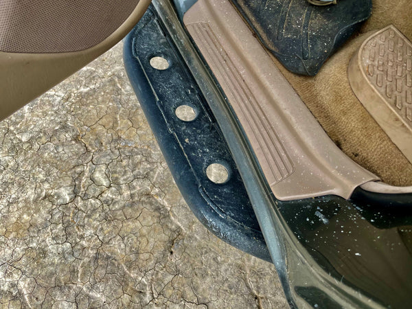 Close-up of black rock slider installed on the side step area of a 100 Series Land Cruiser LX470 with beige interior trim.