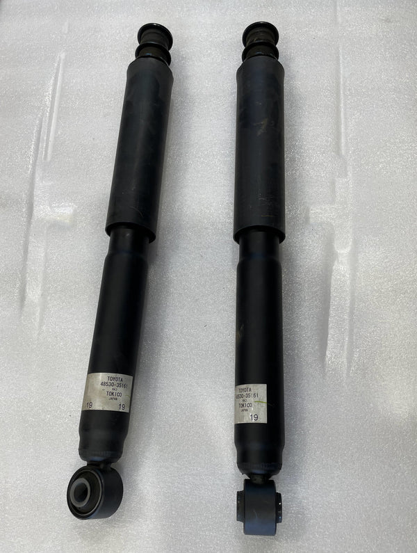 Pair of black stock rear shocks for 5th gen Toyota 4Runner with mounting bushings and labels visible.